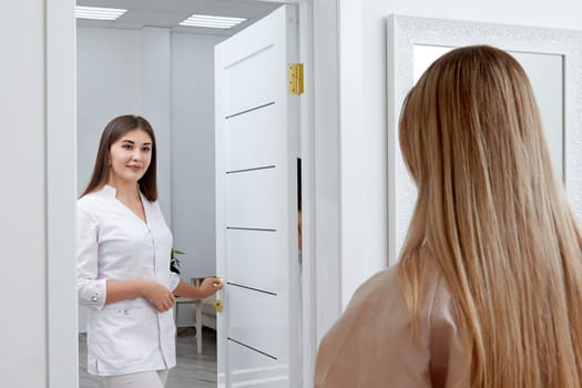 Young female cosmetologist confidently steps into a room where a patient sits in a robe