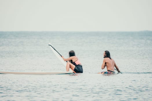Sea woman and man on sup. Silhouette of happy young woman and man, surfing on SUP board, confident paddling through water surface. Idyllic sunset. Active lifestyle at sea or river