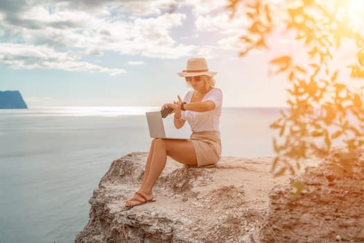 Freelance women sea working on the computer. Good looking middle aged woman typing on a laptop keyboard outdoors with a beautiful sea view. The concept of remote work