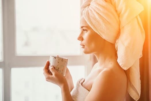 Young serene relaxed woman in spa bath towel drinking hot beverage tea coffee after taking shower bath at home. Beauty treatment, hydration concept