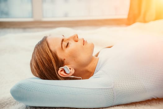 Side view portrait of relaxed woman listening to music with headphones lying on carpet at home. She is dressed in a blue tracksuit