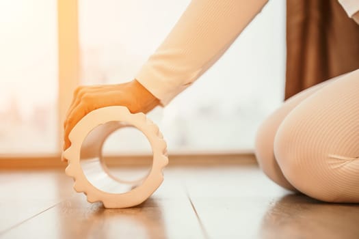 Adult athletic woman, in white bodysuit, performing fascia exercises on the floor - caucasian woman using a massage foam roller - a tool to relieve tension in the back and relieve muscle pain - the concept of physiotherapy and stretching training.