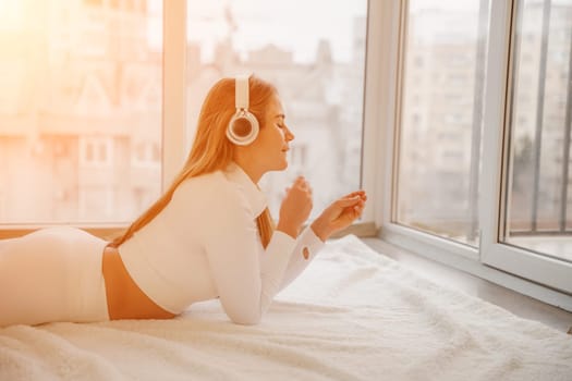 Side view portrait of relaxed woman listening to music with headphones lying on carpet at home. She is dressed in a white tracksuit