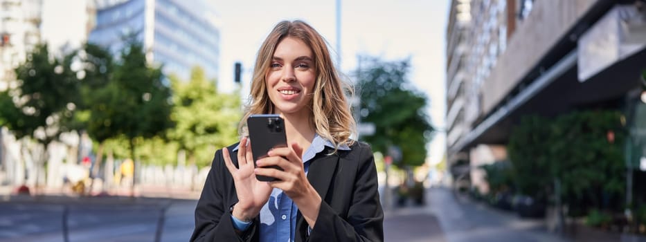 Portrait of smiling businesswoman using mobile phone while standing outdoors near office buildings.