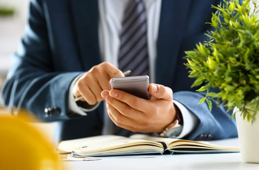 Male arm in suit hold phone and silver pen at workplace closeup. Read news mania send sms chat addict use electronic bank modern lifestyle job plan colleague share blog tweet web application search