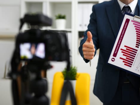 Male in suit and tie show confirm sign arm making promo videoblog or photo session in office camcorder to tripod closeup. Vlogger promotion selfie solution or finance advisor management information
