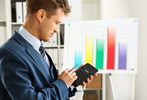 Male arm in suit hold calculator pressing buttons in office closeup. Electronic keypad math data invest credit debit research mortgage loan money saving payment economic debt school