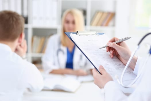 Female medicine doctor hand holding silver pen looking in clipboard pad closeup. Ward round patient visit check 911 medical calculation and statistics concept. Physician ready to examine patient