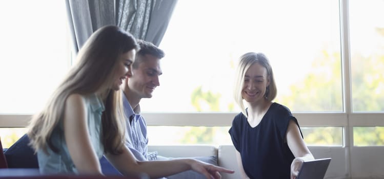 Three young business people in a cafe discussing the problem of teamwork is holding a clipboard. Look smiles and laughing lifestyles are examining documents and laptop.