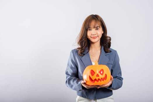Asian woman cradles an orange pumpkin while playfully interacting with it, surrounded by whimsical ghost pumpkins, evoking a sense of Halloween fun and excitement. Halloween Day
