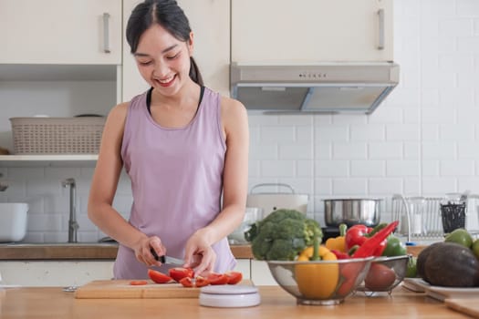 happy young woman cooking healthy vegetarian food at home. Fit smiling housewife or fitness coach in sportswear chopping peppers while making vegetable salad rich in vitamins.