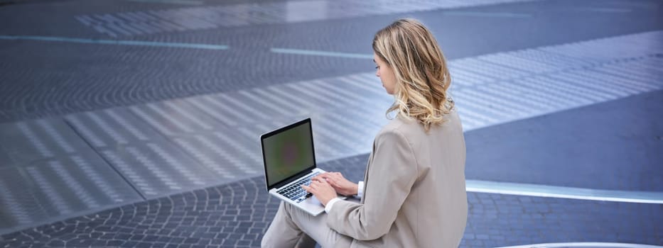 Young digital nomad, businesswoman sitting with laptop in city centre. Office worker using computer outdoors.