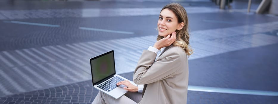 Young digital nomad, businesswoman sitting with laptop in city centre. Office worker using computer outdoors.