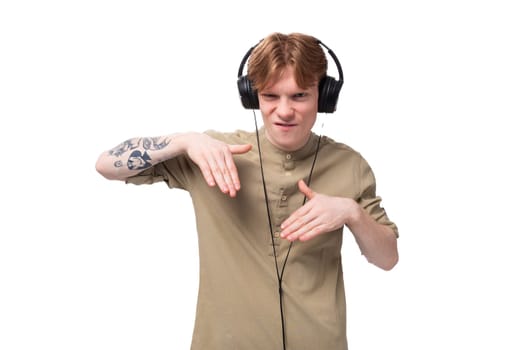 young red-haired man with glasses dressed in a brown shirt grimaces and listens to music on headphones.