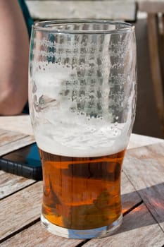 enlish bitter ale with froth of a table in a beer garden next to mobile phone