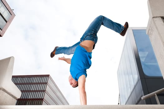 Young man in handstand in front of sky and house front
