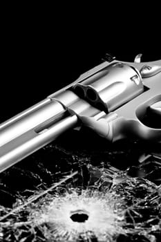 handgun with bullet hole in glass isolated on black - modern revolver with broken glass
