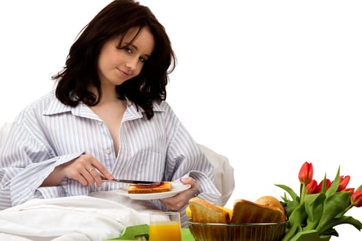 Young woman having breakfast in bed spreading jam on a piece of toast