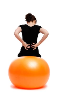 Young woman with back pain sitting on an orange exercise ball