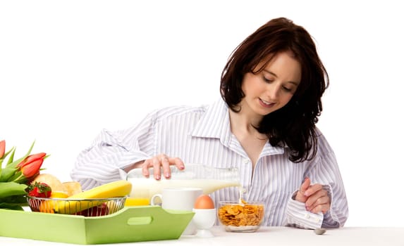 Young pretty woman at breakfast pouring milk in corn flakes