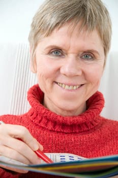 Head and shoulders portrait of a mature woman in a red sweater,puzzle book and pen