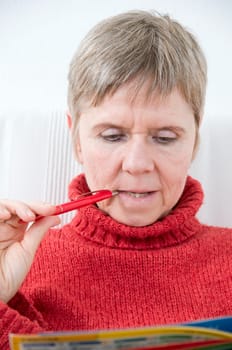 Head and shoulders portrait of a mature woman in a red sweater,puzzle book and pen