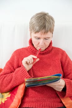 Head and shoulders portrait of a mature woman in a red sweater,puzzle book and pen
