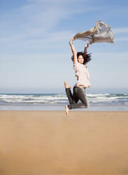 beautiful happy young girl running and jumping over a windy beach with a blowing scarf
