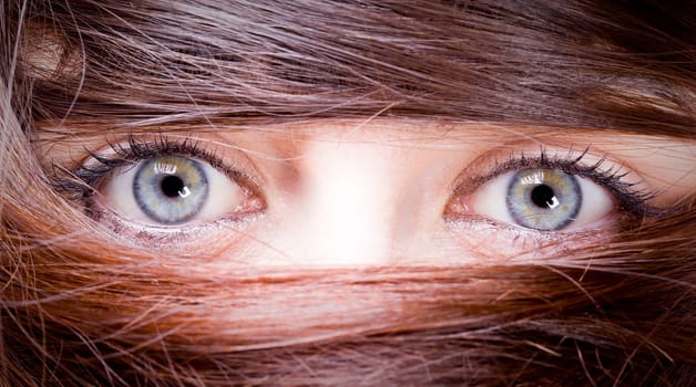 extrange look of a young woman with blue eyes with her hair around the eyes