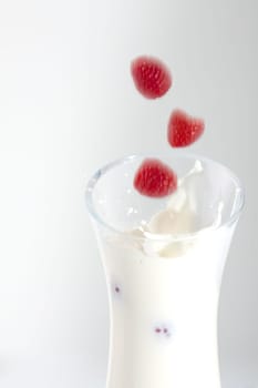 Three raspberries fall into a carafe of milk