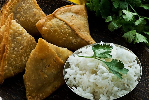 Indian samosa&#039 s on a wooden plate with rice. Garnished with fresh cilantro.