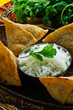 Indian samosa&#039 s on a wooden plate with rice. Garnished with fresh cilantro.