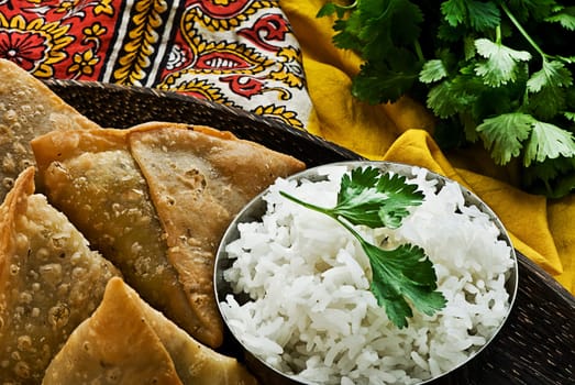 Indian samosa&#039 s on a wooden plate with rice. Garnished with fresh cilantro.