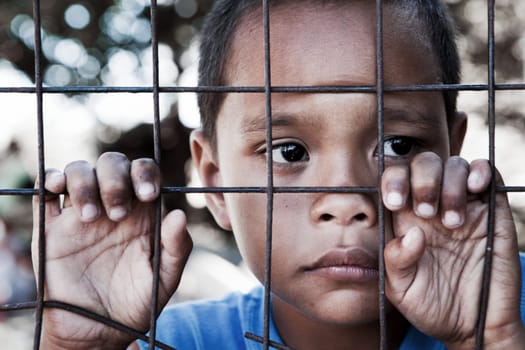 Asian boy behind and clinging to fence in the Philippines - contemplating look to the side - shallow dof with focus on face.