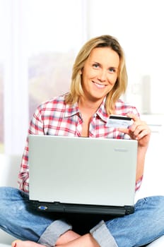 Young woman sitting on sofa with computer and credit card
