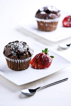 2 plates with chocolate muffins garnished with a strawberry.