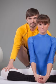 woman in blue leotard and personal trainer helping to do stretching exercises