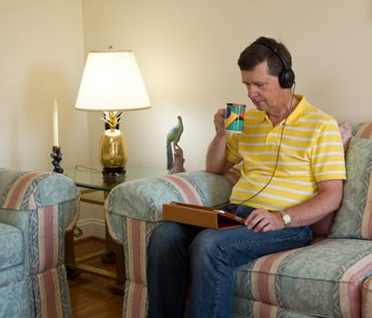 Senior male sitting in modern room and watching from a tablet computer with headphones on his head