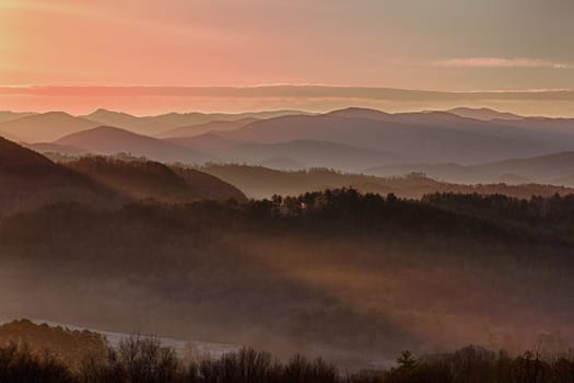 Sun rising over snowy mountains of Smokies in early spring with fog in valleys