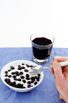 Hand with spoon about to eat a bowl of thawing frozen blueberries with vanilla yogurt, glass of organic blueberry juice.