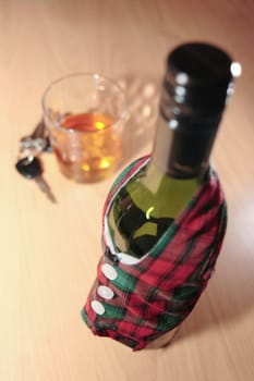 bottle dressed in jacket warmer with car keys on office desk depicting drunk driving and addictions can kill