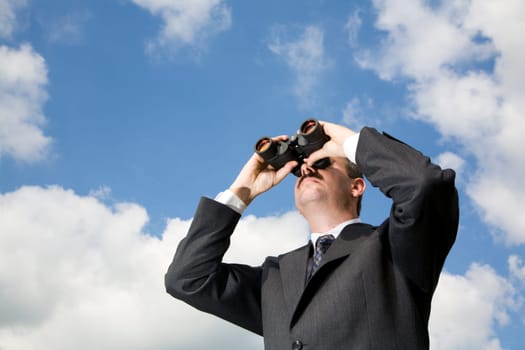 Businessman is looking ahead through binoculars with sky in the background