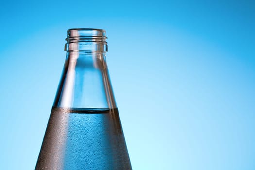 Top portion of bottle with cold water against blue background