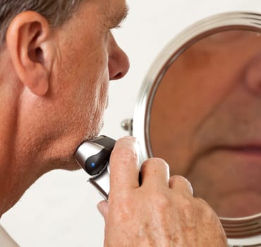 Retired male shaving with electic razor in front of magnifying mirror
