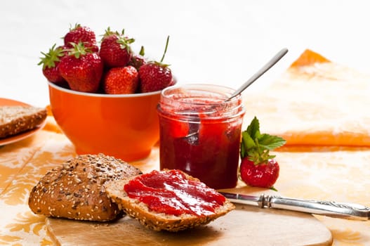 Breakfast table with strawberry jam,rolls,fresh strawberries on breakfast board