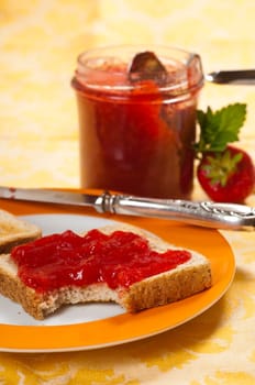 Breakfast table with strawberry jam,toast,fresh strawberries in bowl,porcelain plate