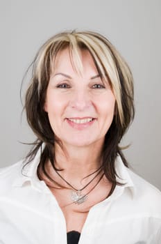 Head portrait of mature blonde woman with dark streaks looking at camera smiling and frontally