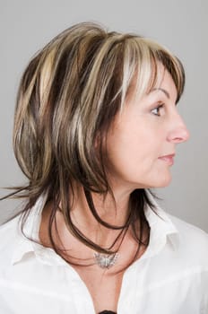 Head portrait of a mature blonde woman with dark streaks looking to the side with head and eyes
