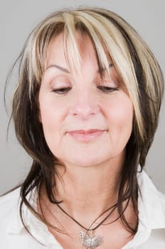 Head portrait of a mature blonde woman with dark streaks looking down only with her eyes