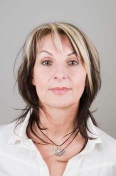Head portrait of mature blonde woman with dark streaks looking head-on at camera with serious expression